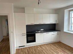 Moderne, neuwertige Einbauküche in Weiß mit dunkler Arbeitsplatte und Holzfußboden.