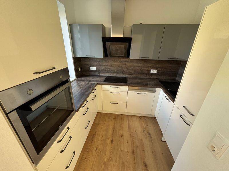 Moderne Einbauküche mit hellen Fronten, Backofen, Kochfeld und Dunstabzugshaube.