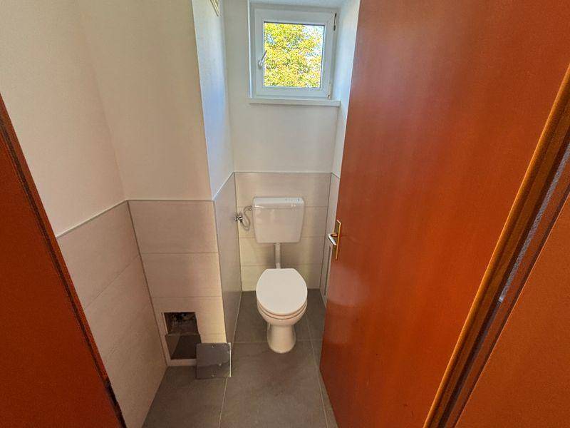 Gäste-WC mit Fenster, Wand-WC und hellen Fliesen an den Wänden.