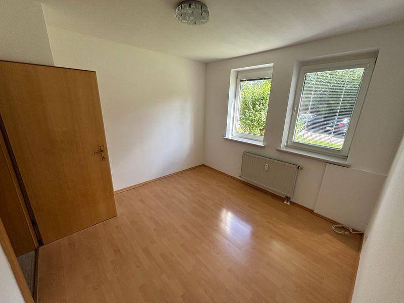 Leeres Zimmer mit Laminatboden, zwei Fenstern und Heizkörper.