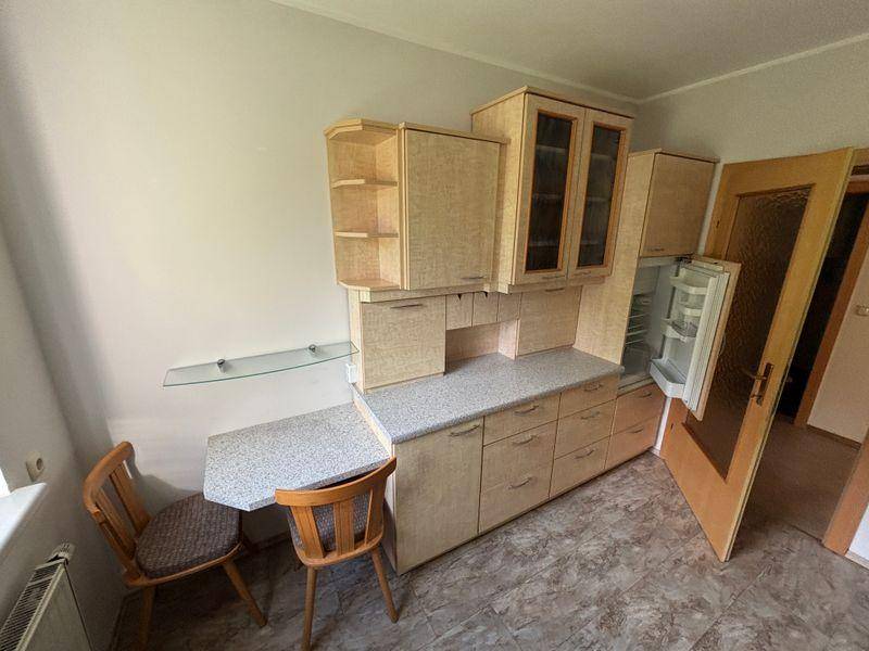Kompakte Einbauküche mit Kühlschrank, hellen Schränken und kleiner Arbeitsfläche.