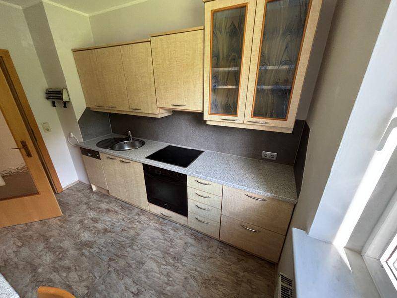 Kleine Küche mit heller Holzoptik, Spüle, Kochfeld und Einbauofen.