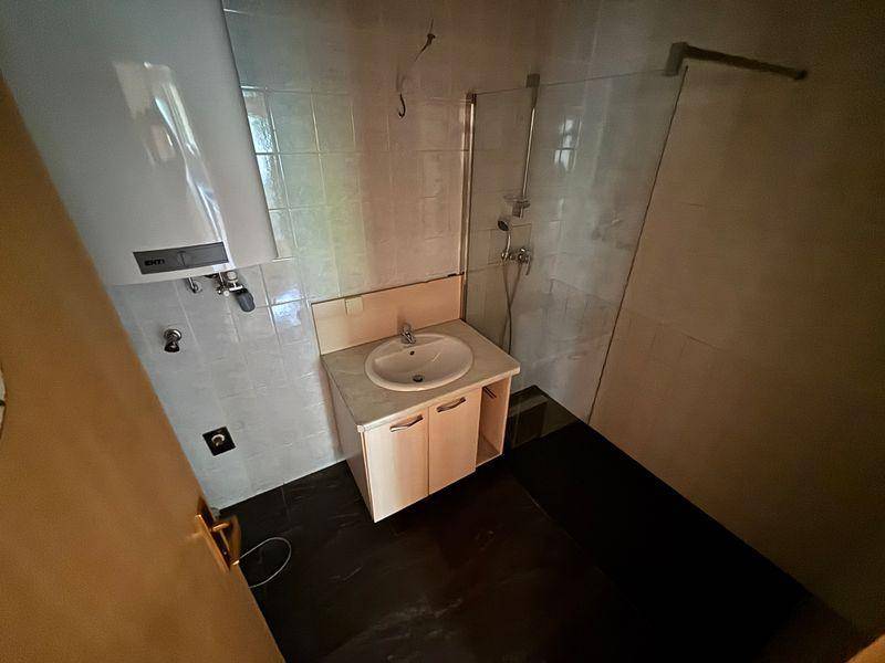 Badezimmer mit Dusche, Waschbecken und Warmwasserboiler.