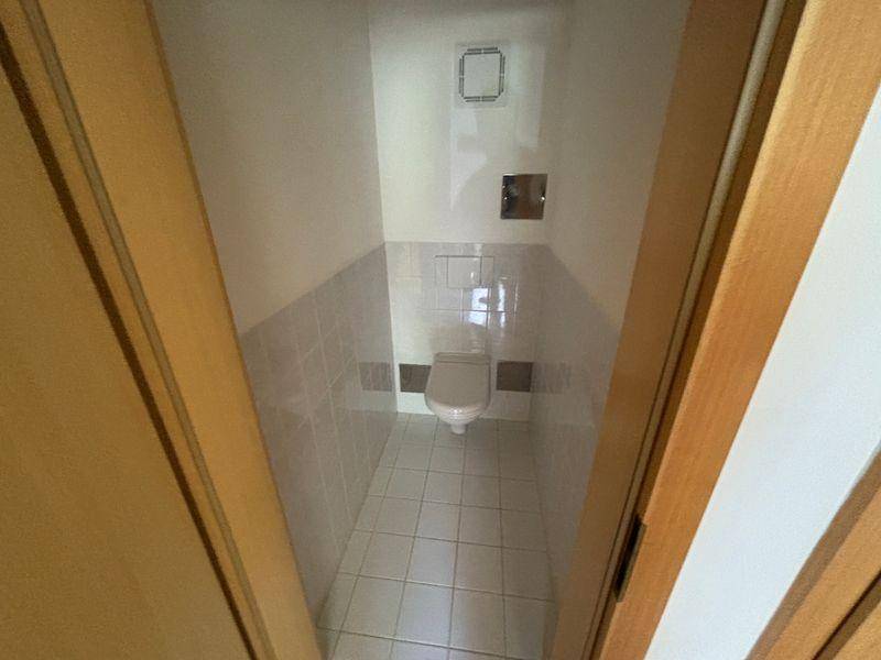 Separates WC mit Wand-WC und hellen Fliesen an den Wänden.