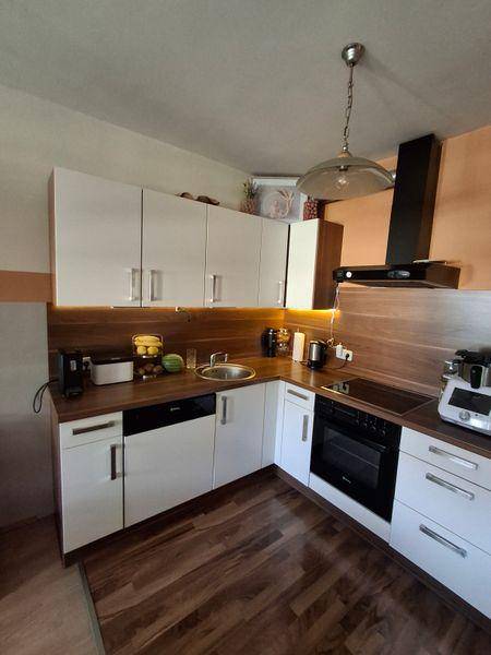 Helle Einbauküche mit weißen Fronten, dunklem Laminatboden und modernen Geräten.