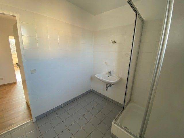 Einfaches Badezimmer mit Duschkabine und kleinem Waschbecken.