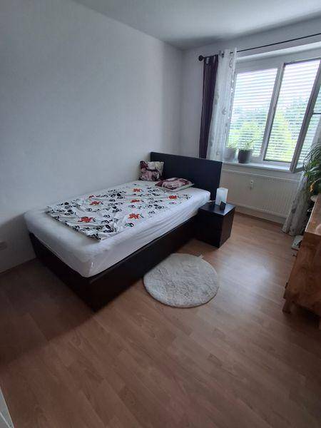Schlafzimmer mit hellem Laminatboden, Einzelbett und Fenster mit Jalousien.