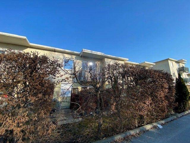 Fassade eines Mehrfamilienhauses mit dichten Hecken im Vordergrund unter blauem Himmel.