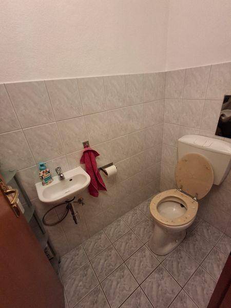 Kleines Gäste-WC mit hellen Fliesen, Wand-WC und einem kleinen Waschbecken.