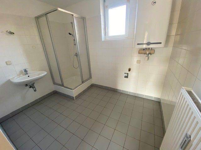 Helles Badezimmer mit Duschkabine, Waschbecken und Fliesenboden.