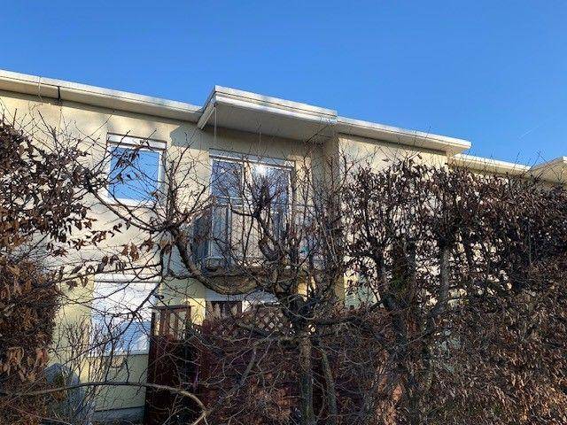 Fassade eines Wohnhauses mit Balkon und großen Fenstern, umgeben von kahlen Bäumen.