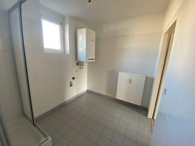 Badezimmer mit Duschkabine, Heizkörper und Gastherme an der Wand.