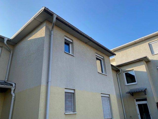 Eckansicht eines Wohnhauses mit Rollläden an den Fenstern unter blauem Himmel.