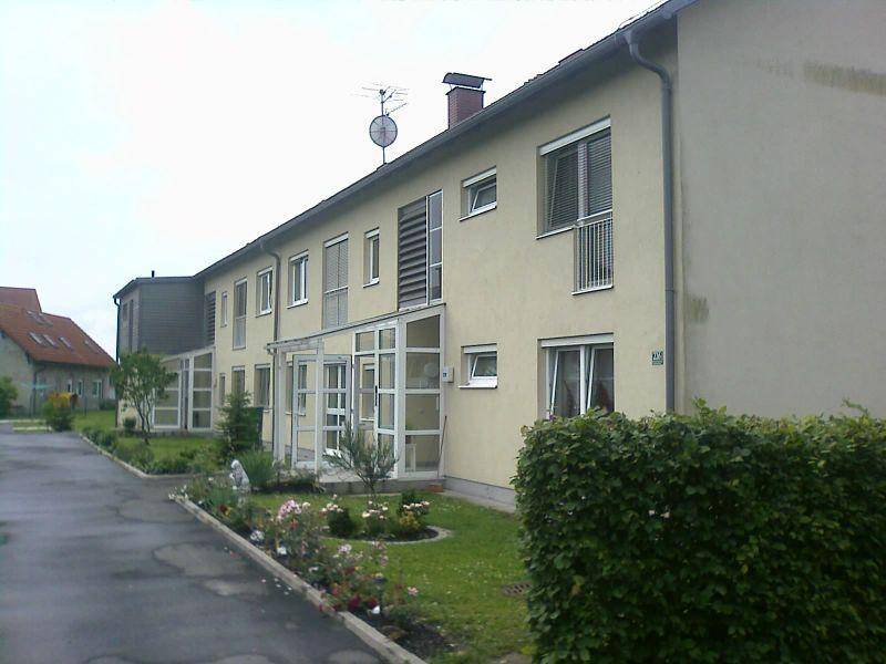 Reihenhäuser mit beiger Fassade, kleinen Vorgärten und Rollläden an den Fenstern.