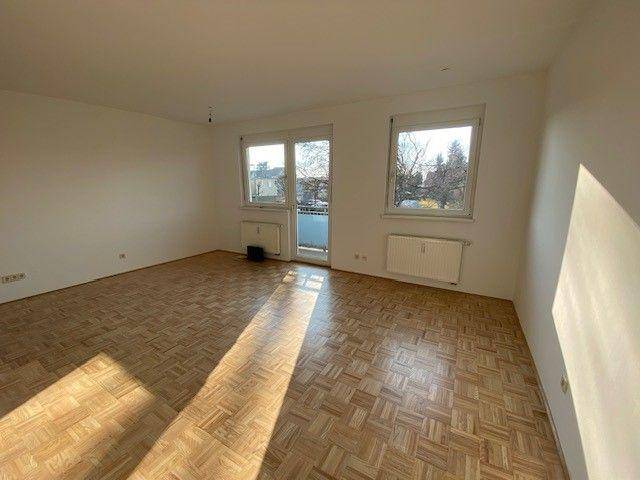 Helles Wohnzimmer mit Parkettboden und Zugang zu einem kleinen Balkon.