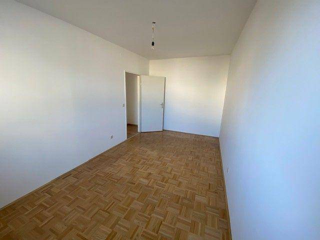 Leeres Schlafzimmer mit Parkettboden und weiß gestrichenen Wänden.