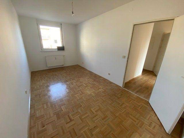 Schlafzimmer mit Parkettboden und Fenster, das viel Tageslicht hereinlässt.