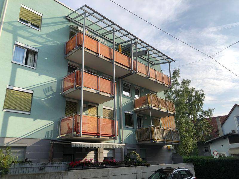 Mehrstöckiges Wohngebäude mit mintgrüner Fassade und mehreren Balkonen mit orangefarbenen Geländern.