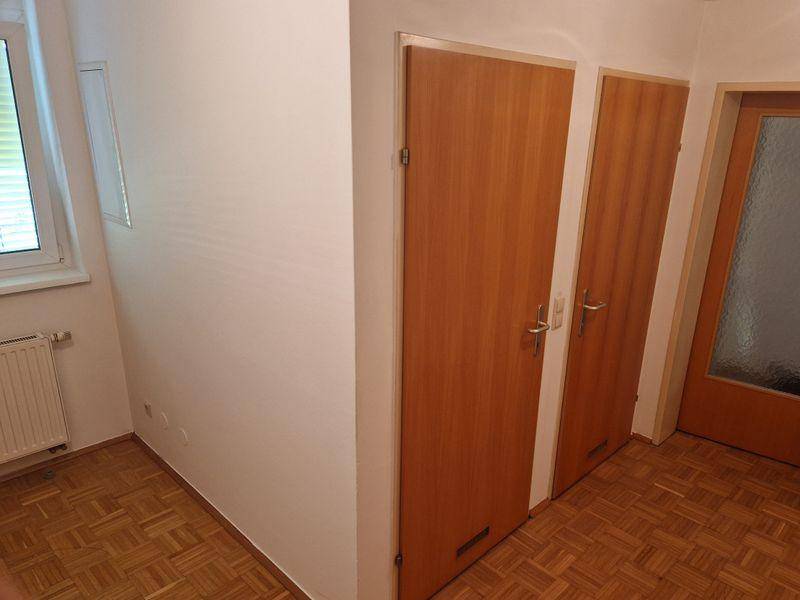 Heller Flur mit Parkettboden, weißen Wänden und Holztüren, der zu weiteren Räumen führt.
