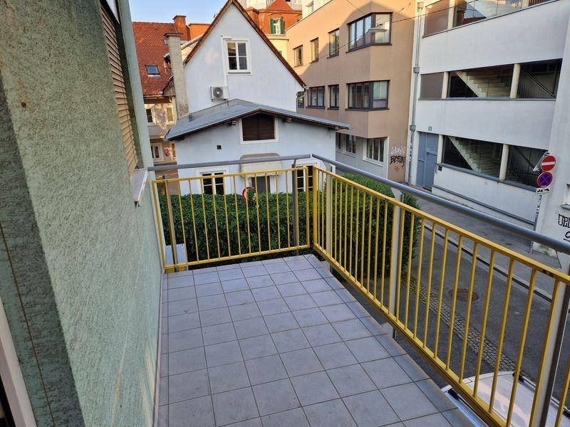 Kleiner Balkon mit Fliesenboden und gelbem Geländer, bietet Blick auf die umliegenden Gebäude.