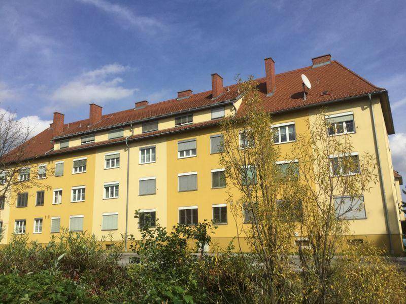 Mehrfamilienhaus mit gelber Fassade, rotem Ziegeldach und Rollläden an den Fenstern.
