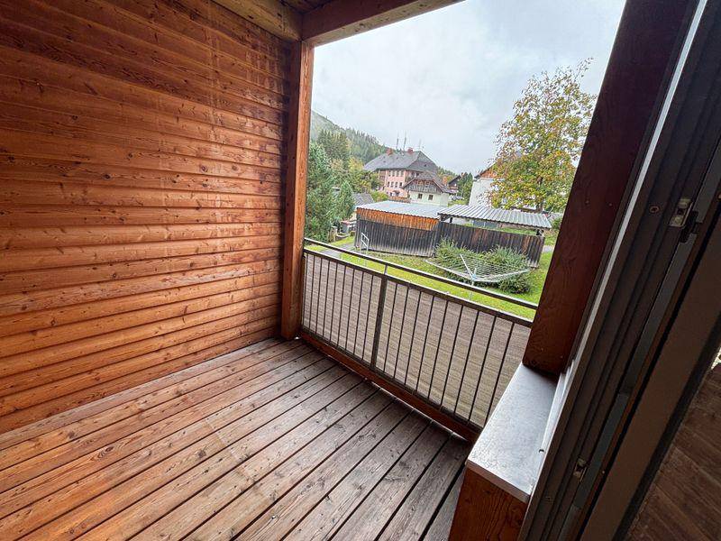 Überdachter Holzbalkon mit Blick auf die grüne Landschaft und umliegende Häuser.