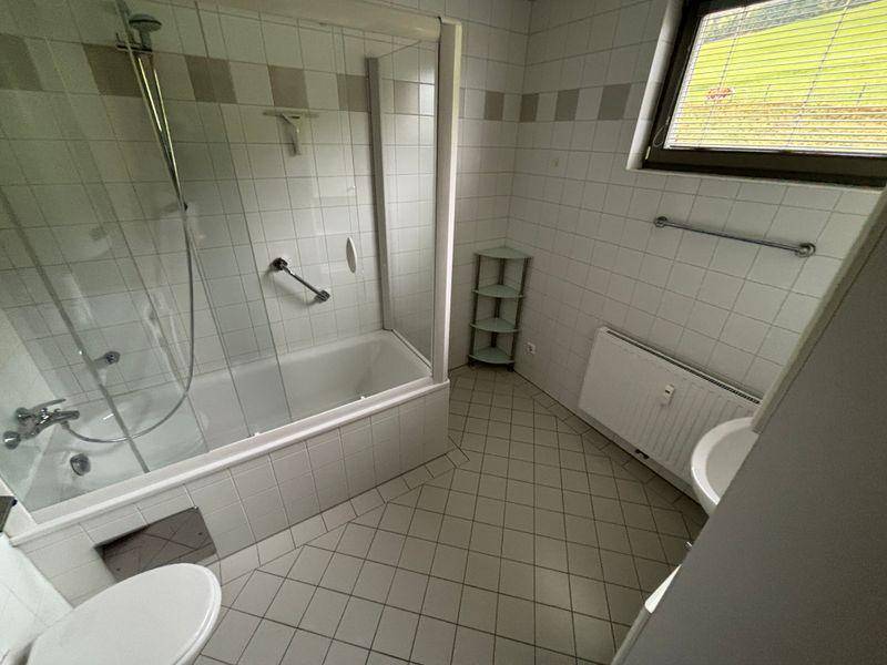 Badezimmer mit Badewanne, Duschabtrennung, Fenster und Haltegriffen.