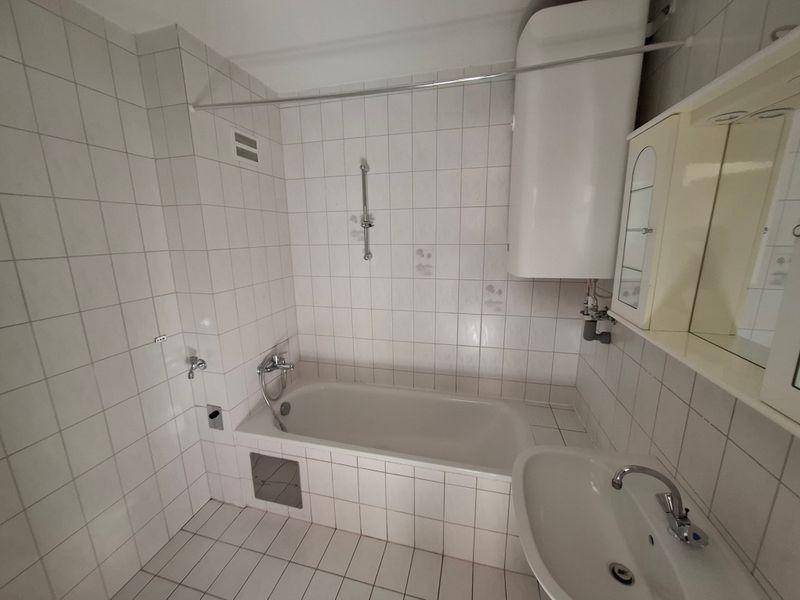 Badezimmer mit weißen Fliesen, Badewanne, Waschbecken und Spiegelschrank, in gutem Zustand.