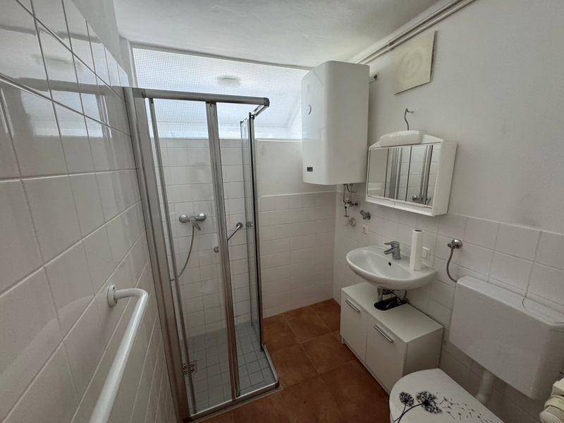 Funktionales Badezimmer mit weiß gefliesten Wänden, Duschkabine und Fenster für Tageslicht.