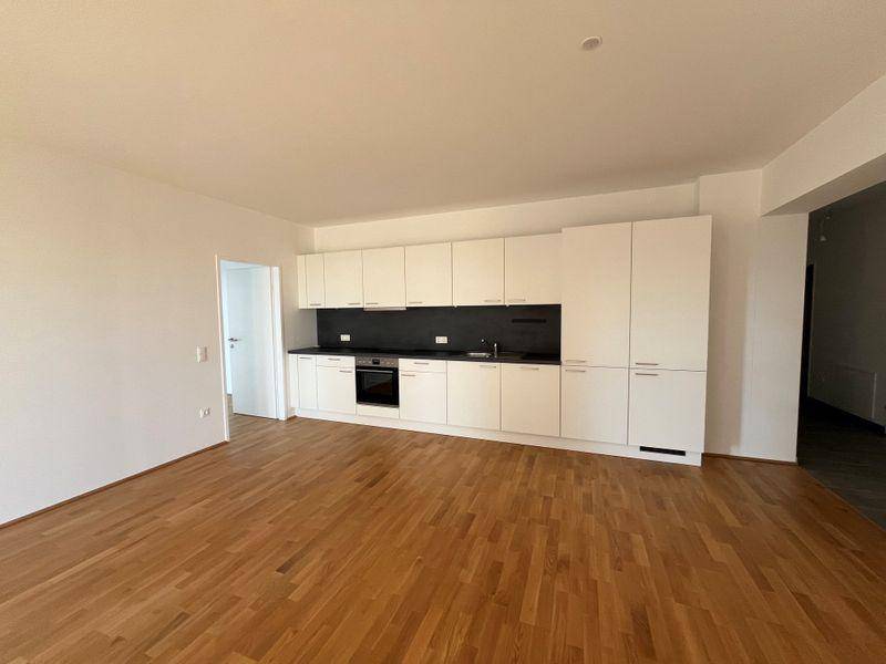 Heller Wohnbereich mit moderner weißer Einbauküche und hochwertigem Parkettboden.