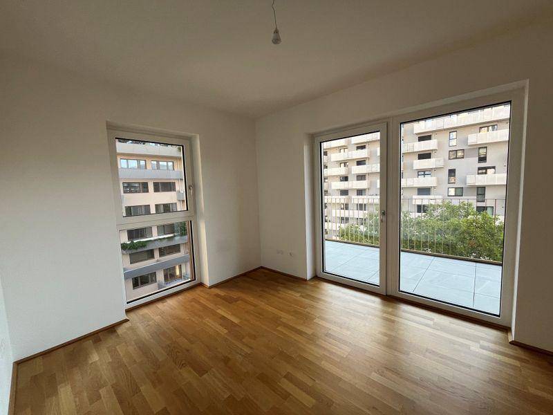 Helles Schlafzimmer mit Parkettboden und großen Fenstern mit Blick auf umliegende Gebäude.