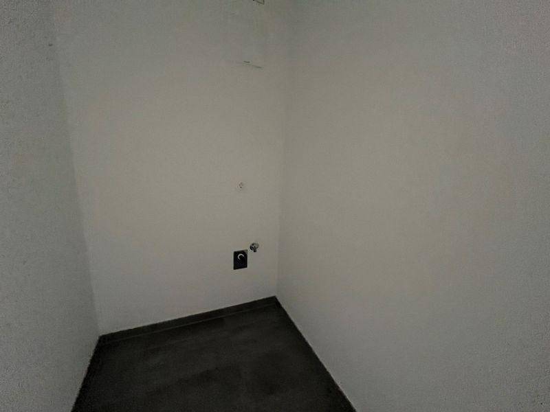Kleiner, leerer Raum mit weißen Wänden und dunklem Fliesenboden, ideal als Abstell- oder Hauswirtschaftsraum.
