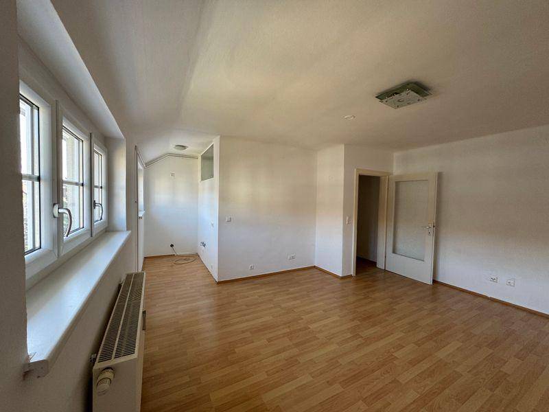 Heller Wohnraum mit Laminatboden, vielen Fenstern und schrägen Decken im Dachgeschoss.