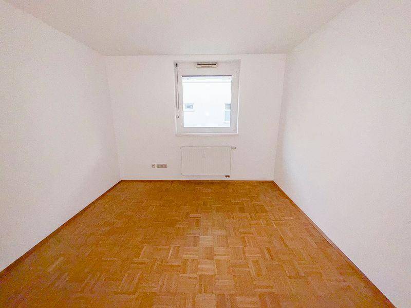 Helles Schlafzimmer mit Parkettboden und einem Fenster mit Blick nach draußen.