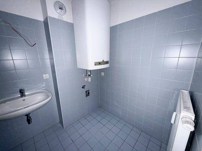 Badezimmer mit Waschbecken, Boiler und Heizkörper, komplett gefliest in Hellblau.