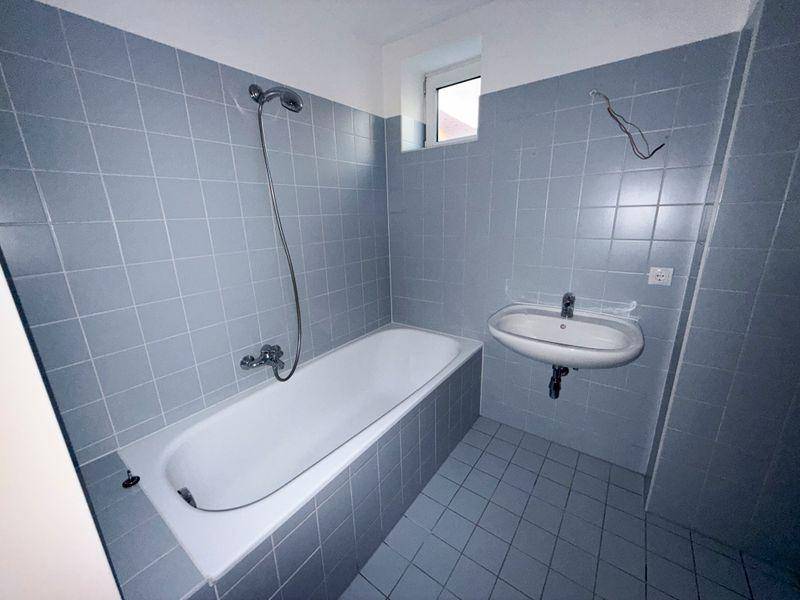 Badezimmer mit Badewanne, Waschbecken und hellblauen Fliesen an Wänden und Boden.