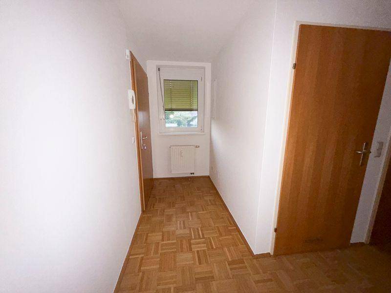 Heller Flur mit Parkettboden, einem Fenster und einer Heizung unter dem Fenster.