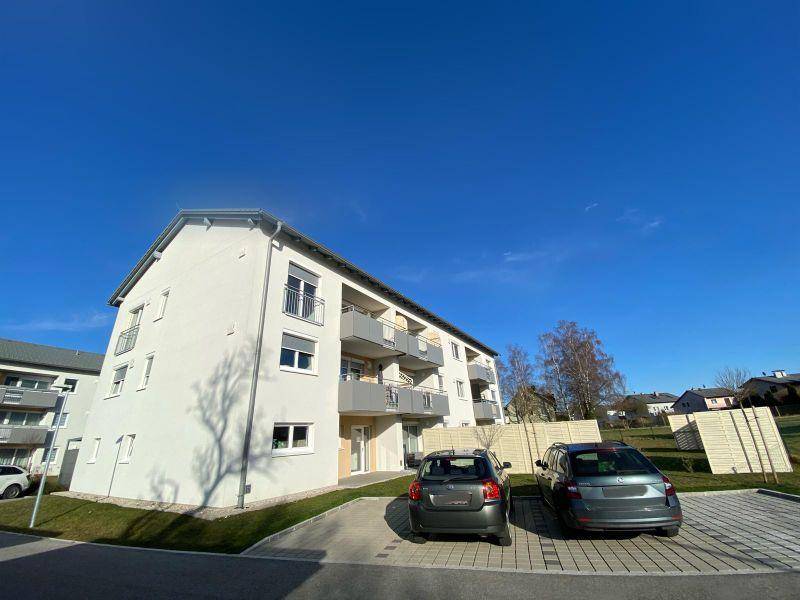 Modernes Neubau-Wohngebäude mit zeitgenössischer Architektur, Balkonen und Außenparkplätzen unter blauem Himmel.
