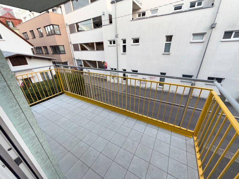 Balkon mit gelbem Geländer und Fliesenboden, bietet einen Blick auf die Straße und Gebäude.