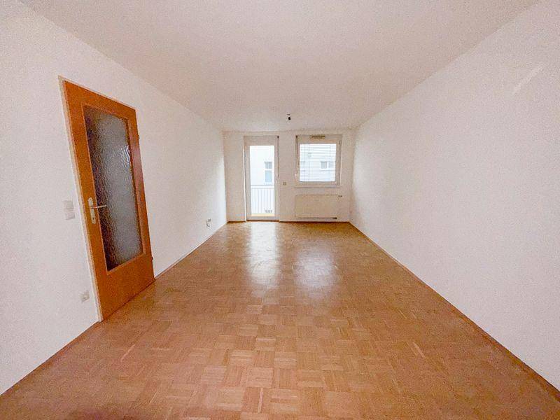 Helles Wohnzimmer mit Parkettboden und Fenstern, die viel Tageslicht hereinlassen.