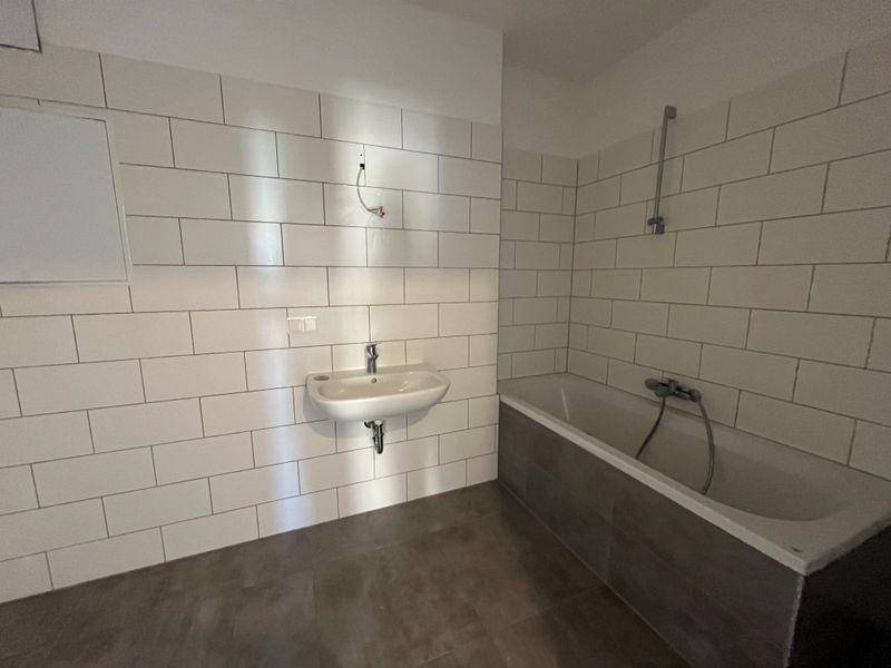 Modernes Badezimmer mit weißen Fliesen, Waschbecken und einer Badewanne.