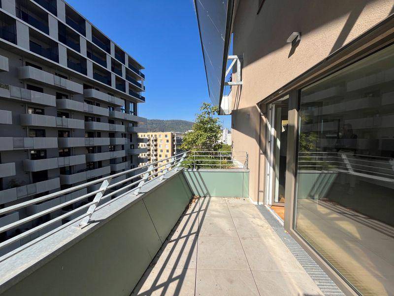Geräumiger Balkon mit Fliesenboden und Metallgeländer, umgeben von anderen Gebäuden.