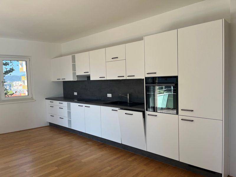 Moderne Einbauküche mit weißen Schränken, dunkler Arbeitsplatte und integriertem Backofen.