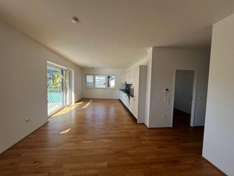 Geräumiger, heller Wohnbereich mit Holzboden und Zugang zu einem Balkon.