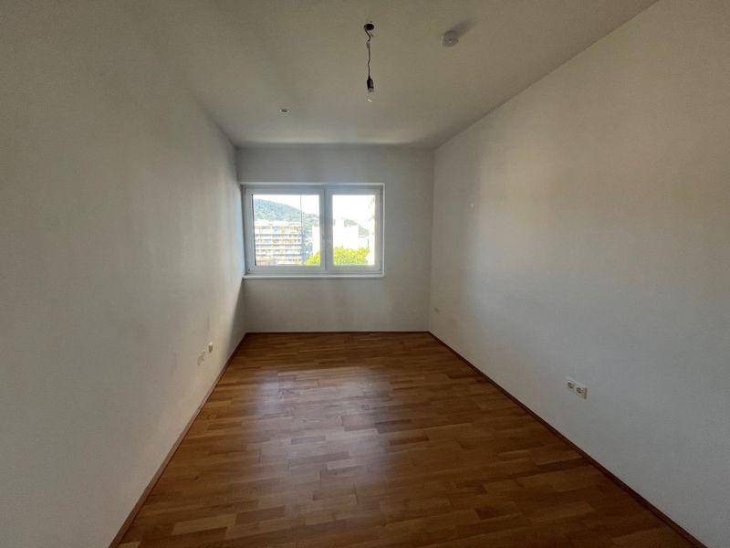 Helles Schlafzimmer mit Holzboden und einem Fenster mit Blick ins Grüne.