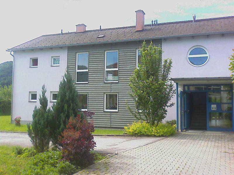 Eingangsbereich eines Wohngebäudes mit moderner Fassadengestaltung und kleinen Bäumen im Vorgarten.