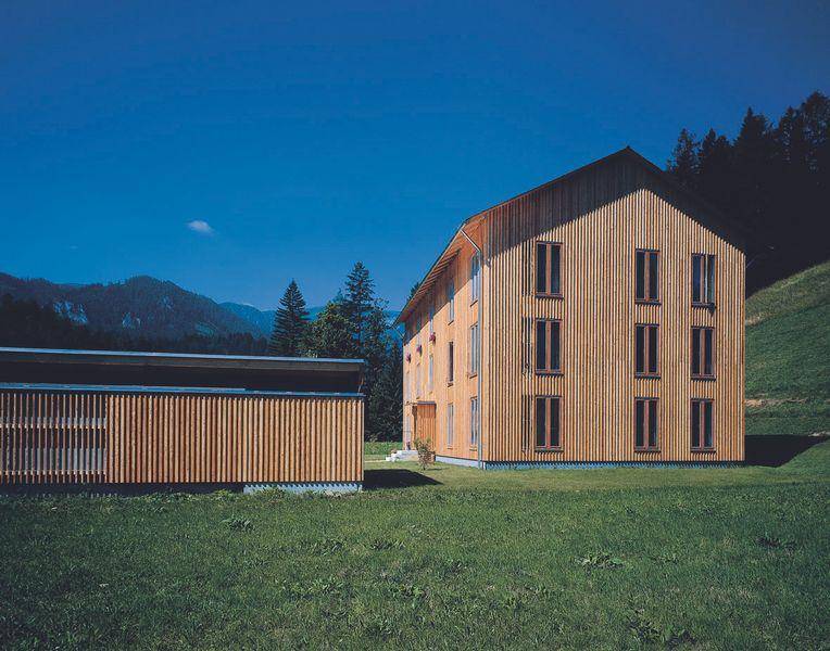 Architektonisch ansprechendes Holzgebäude in ländlicher Umgebung mit Bergblick unter blauem Himmel.