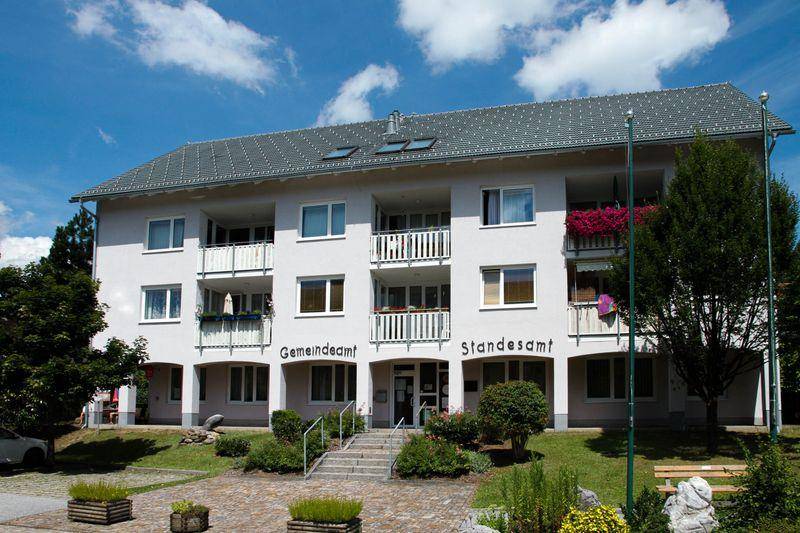 Mehrfamilienhaus mit weißer Fassade, Satteldach und Balkonen, umgeben von Grünflächen.