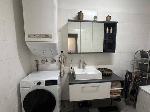 Helles Badezimmer mit Waschbecken, Spiegelschrank, Boiler und Waschmaschine.