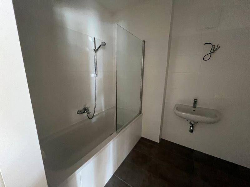 Badezimmer mit Badewanne, Duscharmatur und Glasabtrennung sowie einem kleinen Waschbecken.